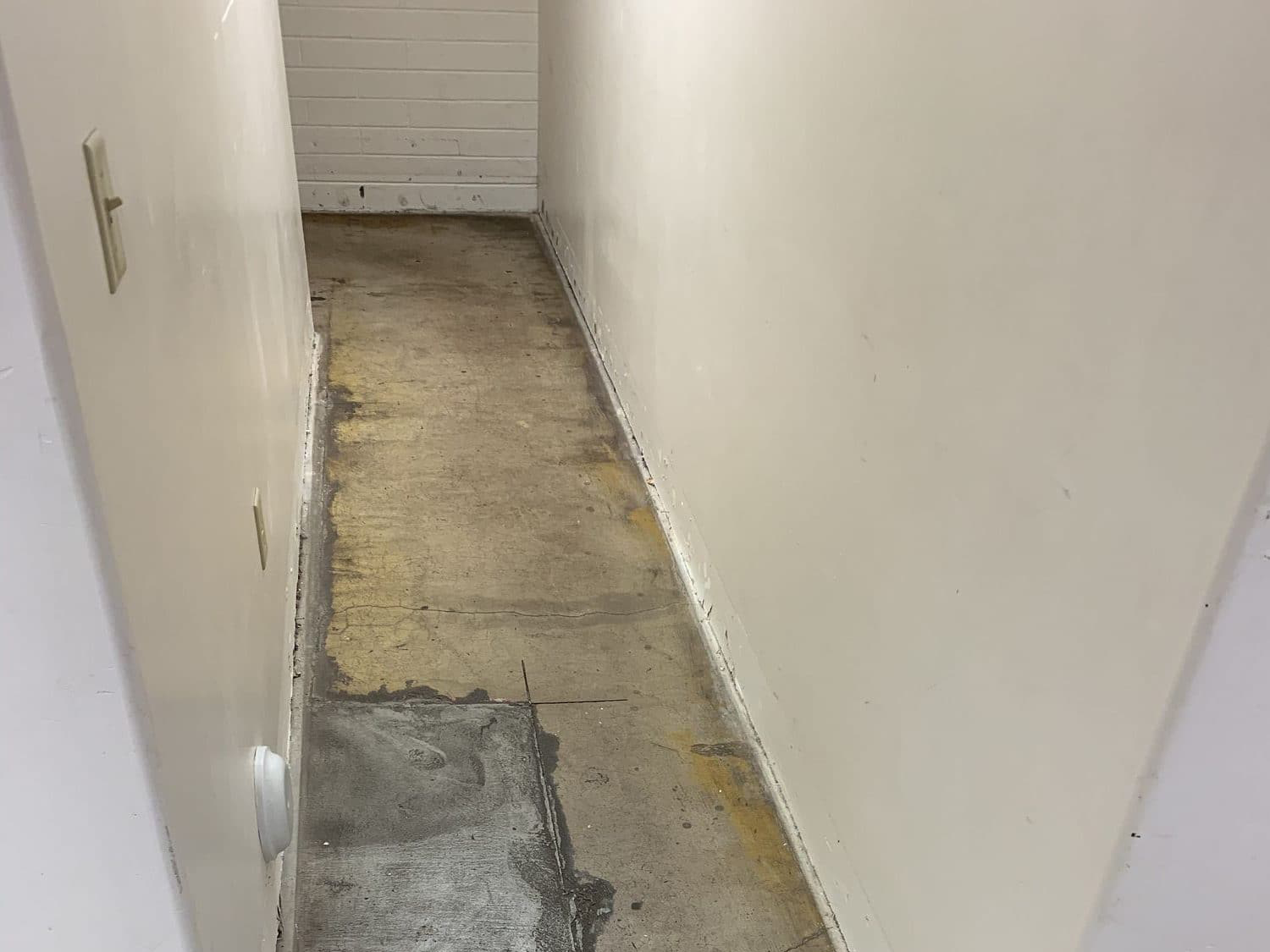 A before photo of a rugged-looking concrete floor in a white basement.