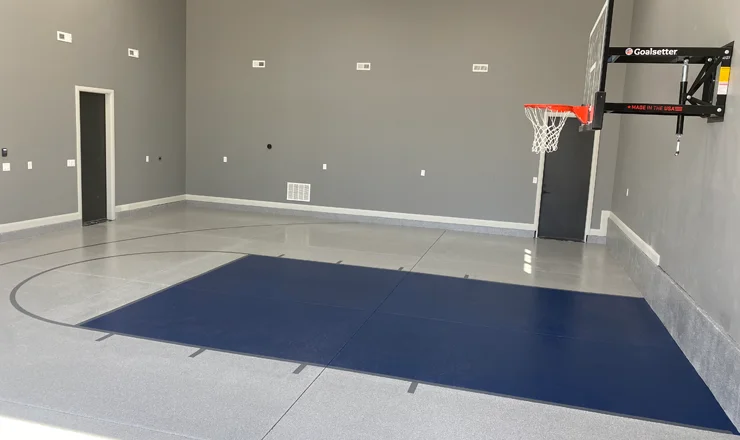 A small sports room with gray walls, a blue mat, and a polished concrete floor.