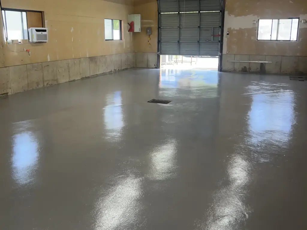 An after photo of an empty warehouse with a fully polished and coated concrete floor with a large aluminum roller door.