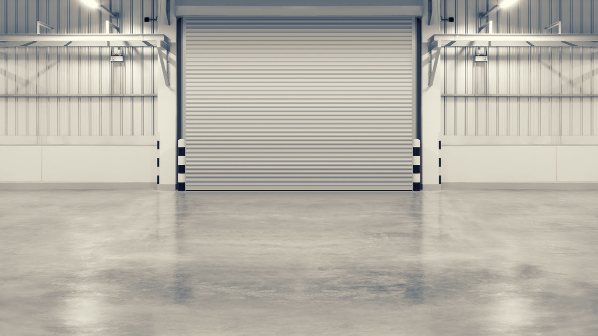 A fully polished, gray concrete floor with an aluminum roller door in a large warehouse.