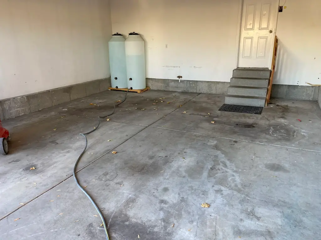 A before photo of a warehouse with unpolished concrete floor and two water tanks connected to a hose.
