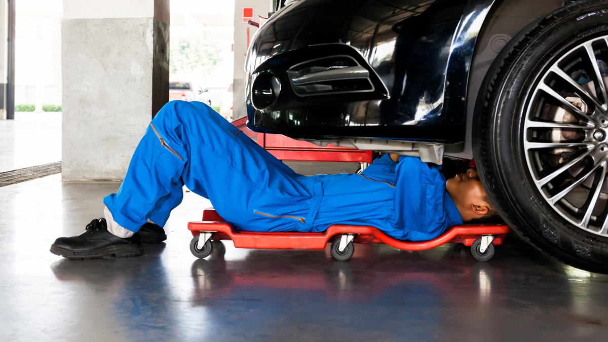 A mechanic working under a car in a garage with concrete flooring.