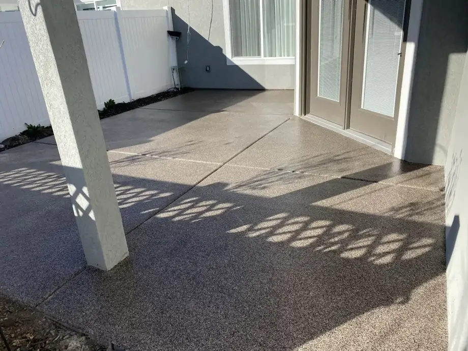 A concrete, tiled patio of a gray house with a gray door.