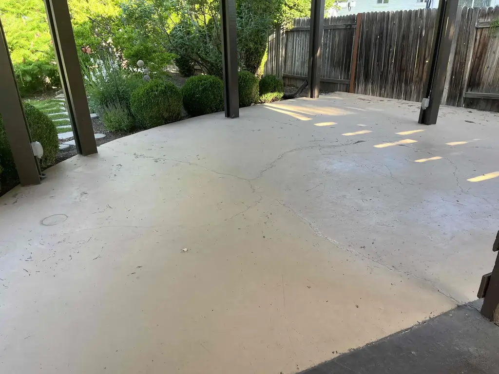 A before photo of a rugged concrete patio connected to a lush garden.