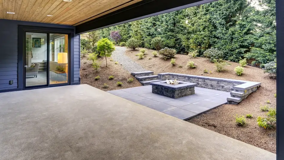 A modern backyard with sliding glass doors, a concrete flooring, and a concrete fire pit area.