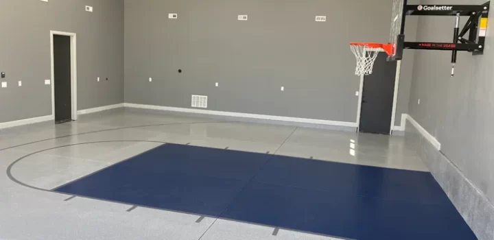 A small sports room with gray walls, a blue mat, and a polished concrete floor.